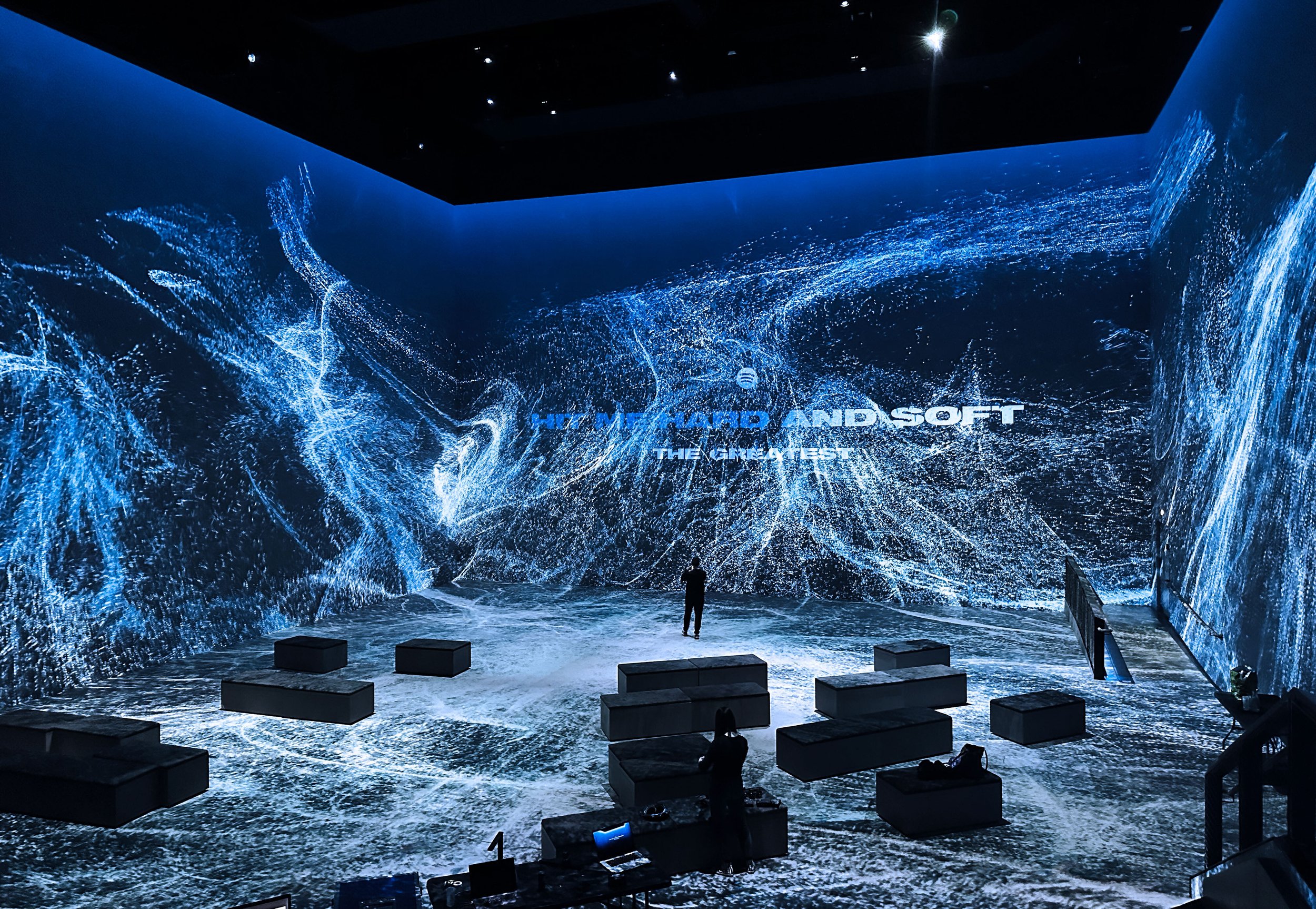 A person standing before a large digital display with swirling blue and white abstract visuals and the words 'THE FUTURE AND SOFT THE ENTERPRISE' in the background.